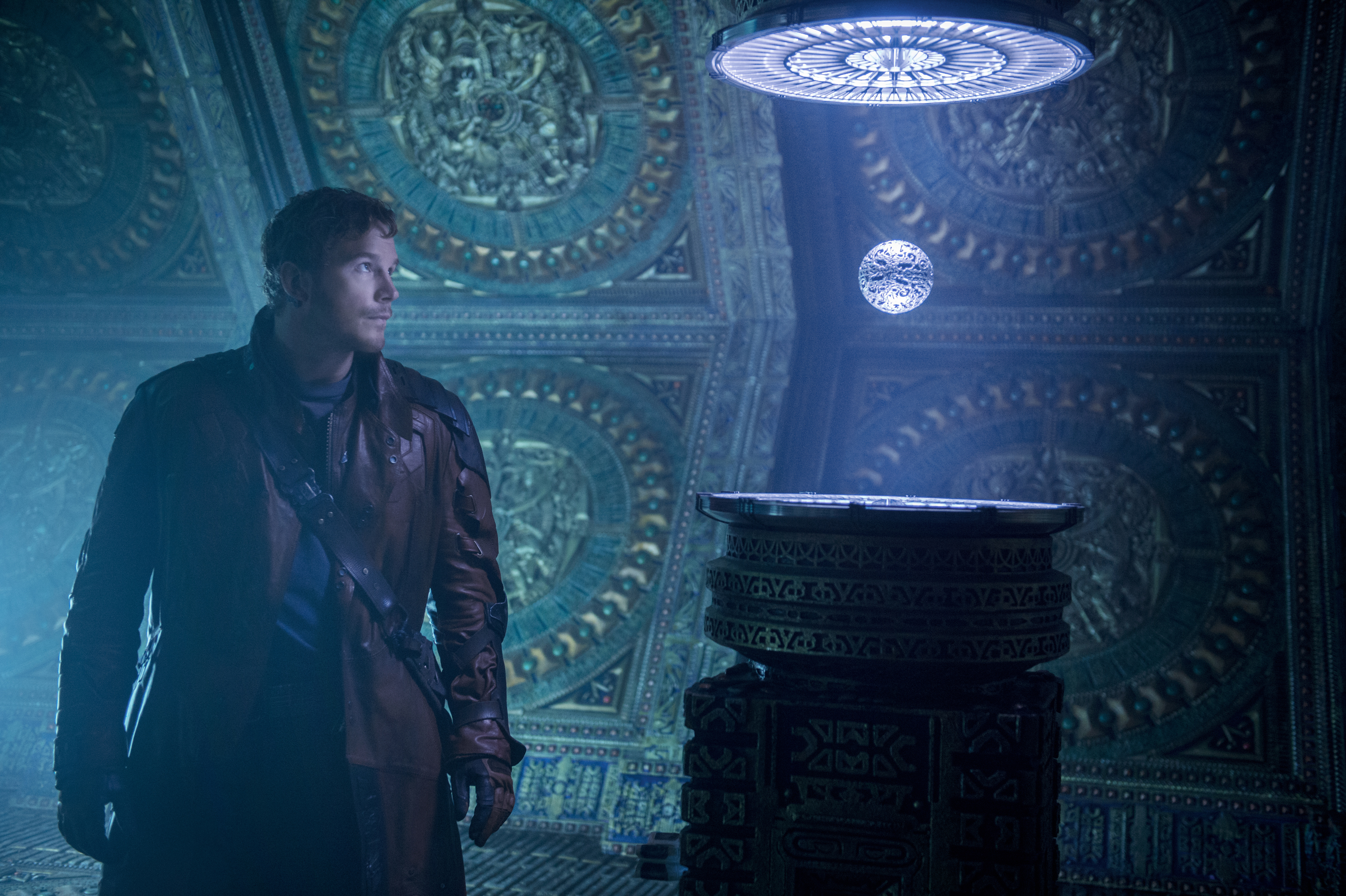 Filmszene: Mann in einem Mantel, der einen schwebenden Orb in einem futuristischen Raum betrachtet.