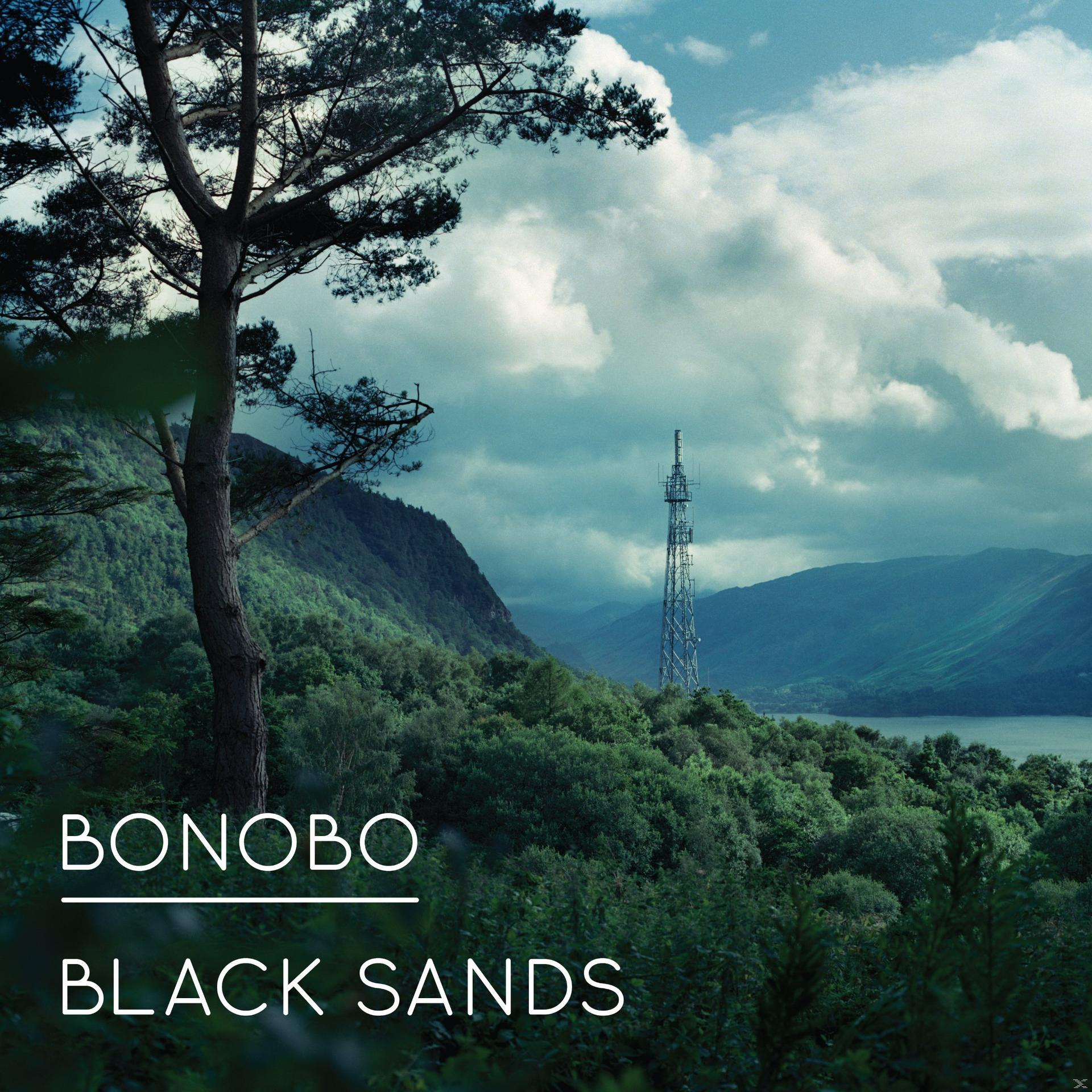 Landschaft mit hohem Baum, grünen Hügeln und einem Telekommunikationsturm unter bewölktem Himmel. Text "BONOBO BLACK SANDS".