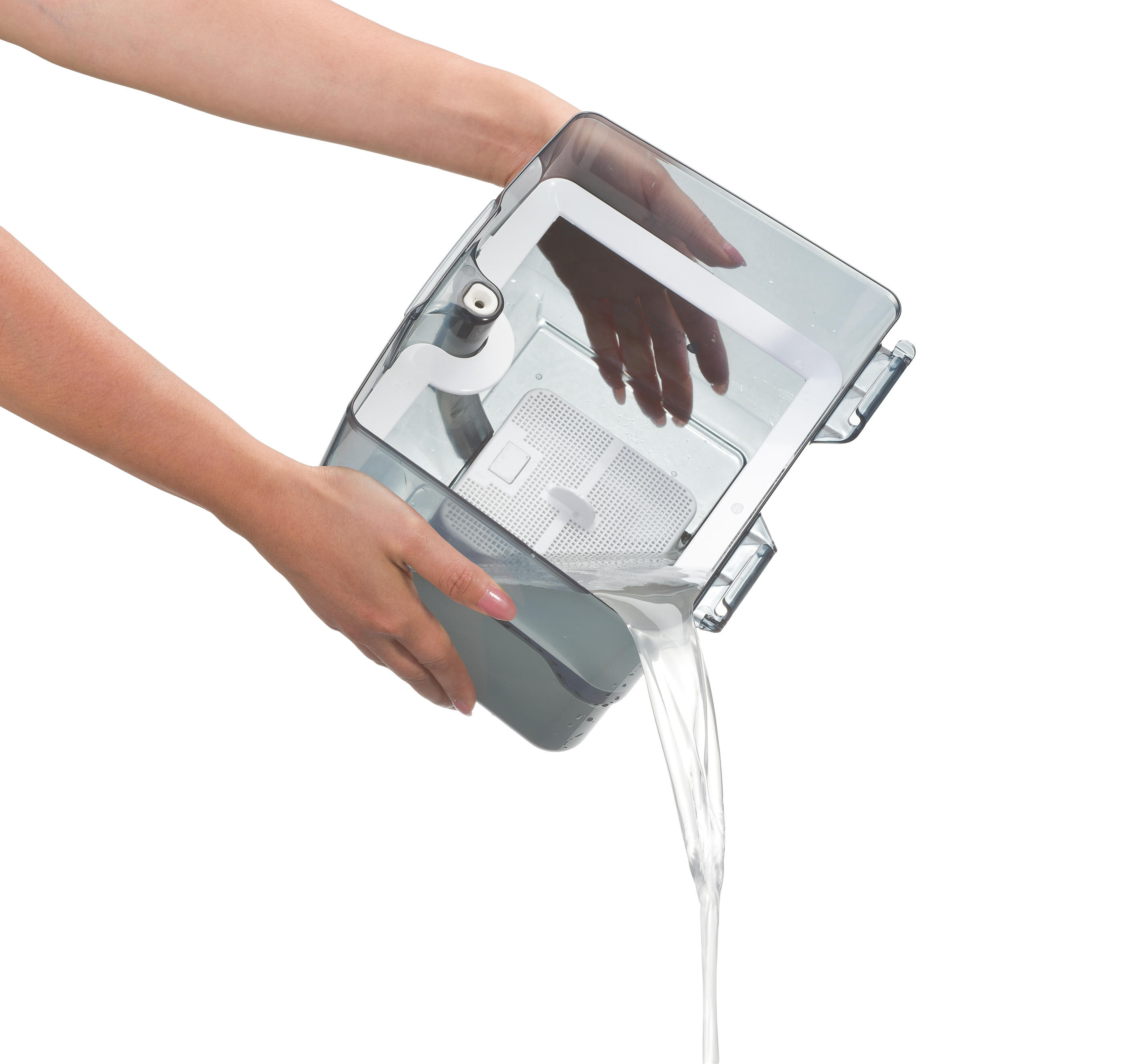 Hände, die Wasser aus einem transparenten Behälter gießen. Der Behälter befindet sich über einer hellen Oberfläche.