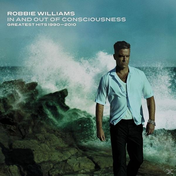 Robbie Williams egy sziklás parton áll, mögötte viharos tengerrel.