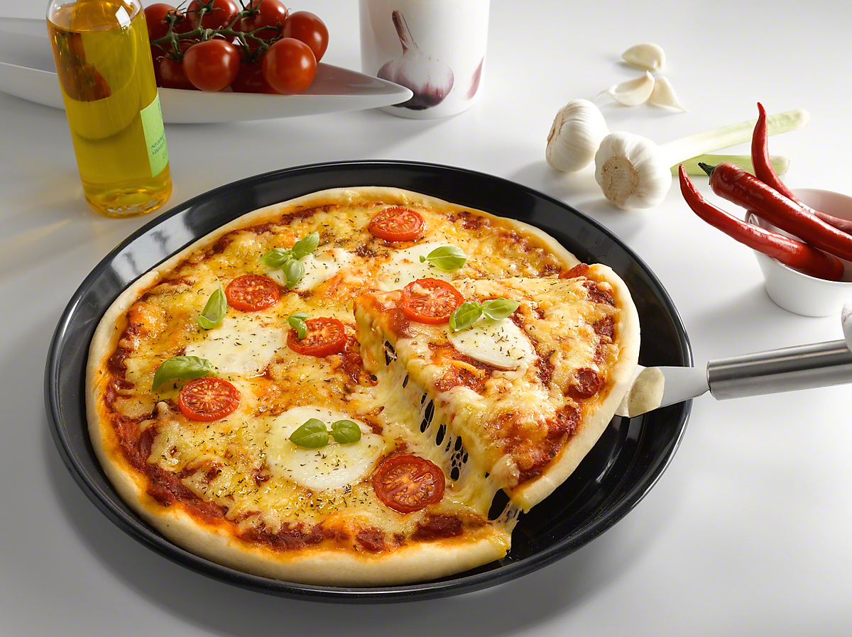 Pizza mit Tomaten und Mozzarella. Ein Stück wird mit einem Pizzaserver angehoben. Andere Zutaten.