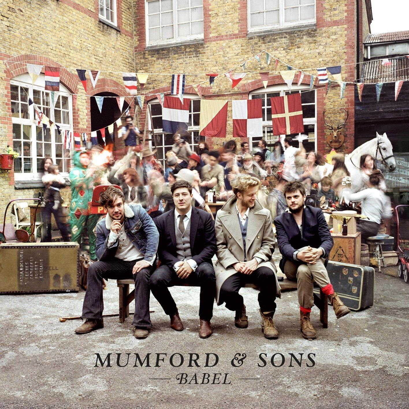 Mumford & Sons albumhoes: vier mannen zitten, vage menigte achter, banners boven, voor een gebouw.
