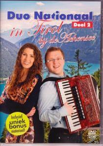 Man speelt accordeon, vrouw lacht. Bergen op achtergrond.