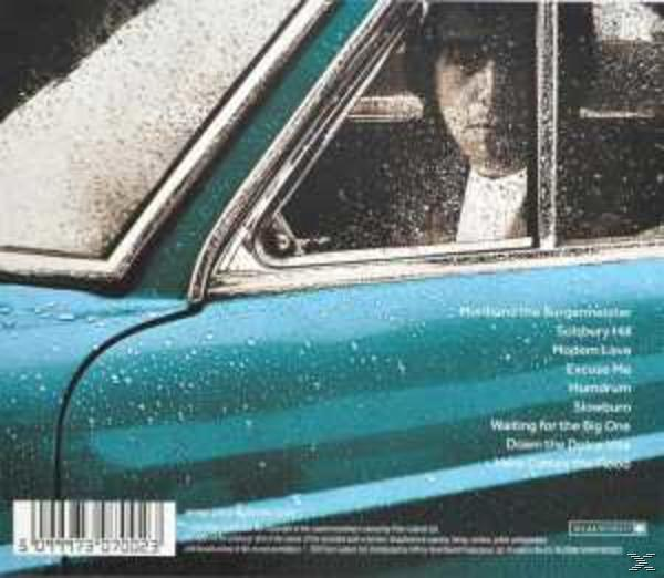 Rückseite einer CD. Ein Mann sitzt in einem blauen Auto. Unten steht Text.