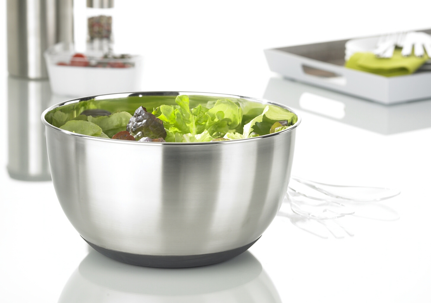 Eine Salatschüssel aus Edelstahl, gefüllt mit grünem Salat, mit Servierutensilien.