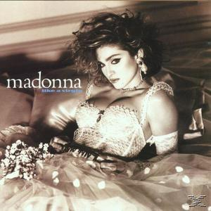 Madonna auf einem Bett, trägt ein weißes Spitzenkleid mit Blumenstrauß.