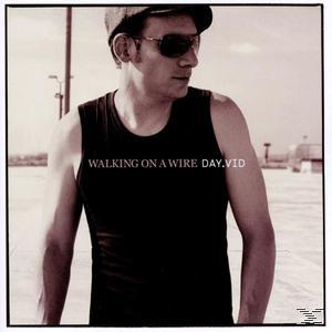 Ein Mann in einem schwarzen Tanktop und Sonnenbrille, mit Text 'Walking on a Wire Day.vid'.