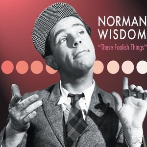 Norman Wisdom im Anzug und Hut, blickt nach oben. Roter Hintergrund mit weißen Punkten.