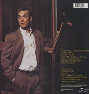 Ein Mann im Anzug steht neben einer Holztafel mit Albumdetails und blickt nach links.