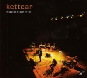 Live-Konzertbühne mit einer Band, die spielt. Kettcar-Bandname oben. Dunkle Beleuchtung.