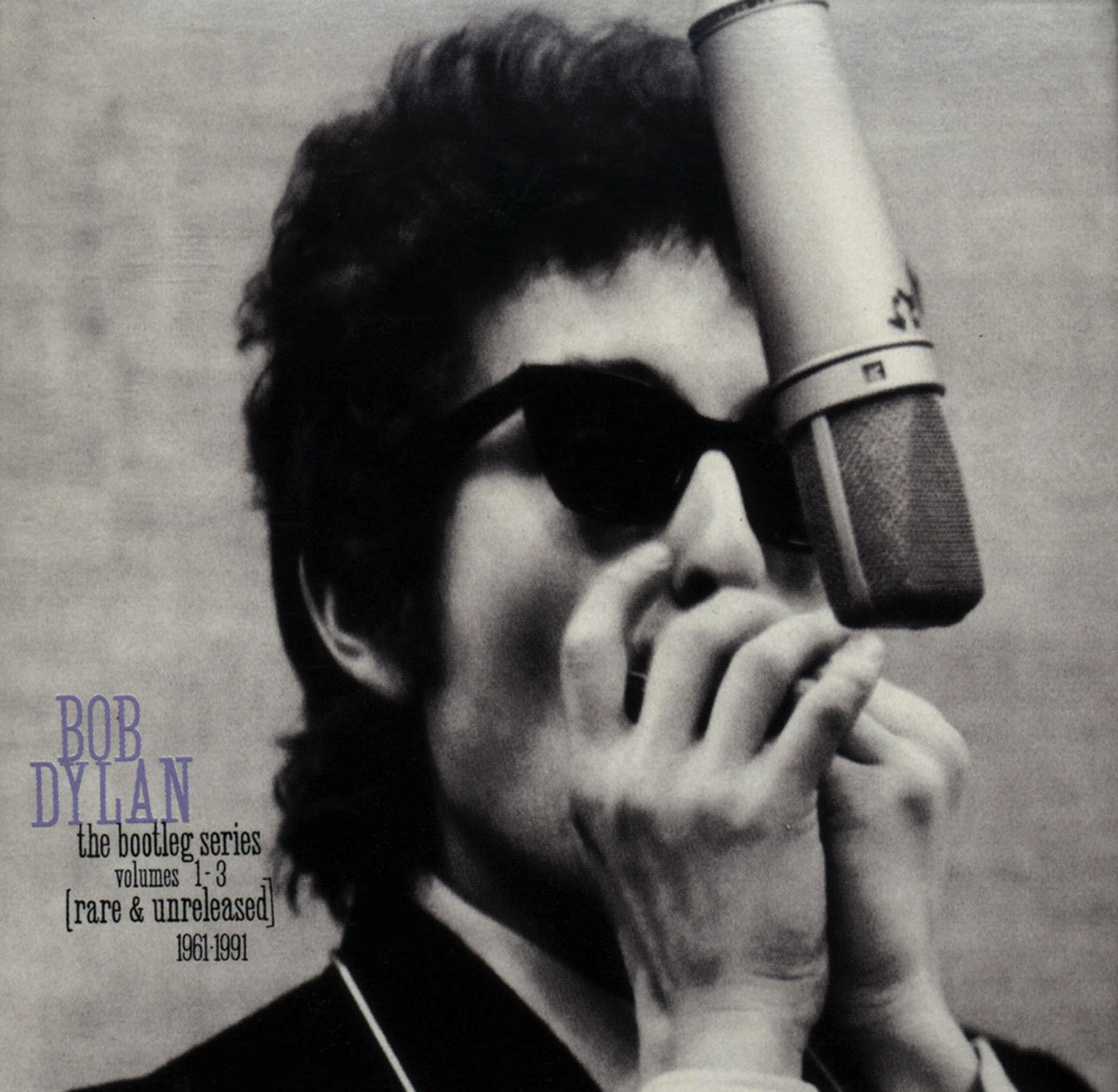 Bob Dylan in Graustufen, Sonnenbrille, Mikrofon. Albumcover für 'The Bootleg Series'.