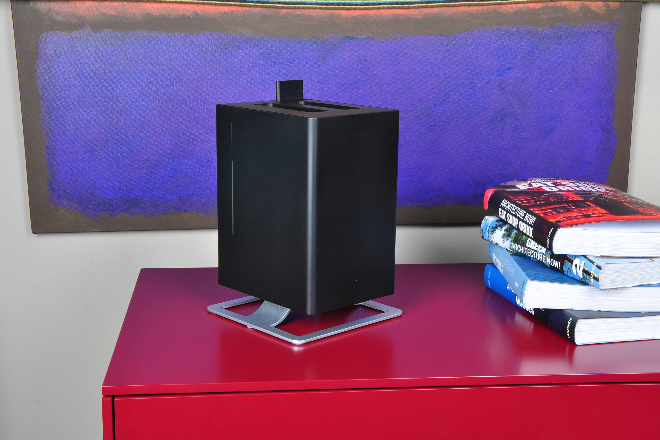 Ein schwarzes Würfelgerät auf einem roten Tisch, mit einem großen abstrakten Gemälde im Hintergrund.