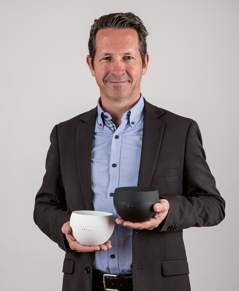 Ein Mann hält eine weiße und eine schwarze Schale und lächelt in die Kamera.