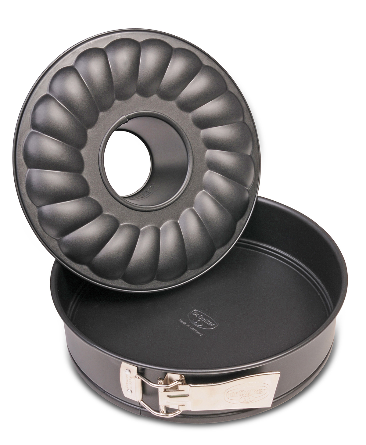Eine schwarze Gugelhupf-Form mit geriffeltem Design, Deckel abgenommen, neben einem runden Boden. Metallgriff an der Seite sichtbar.