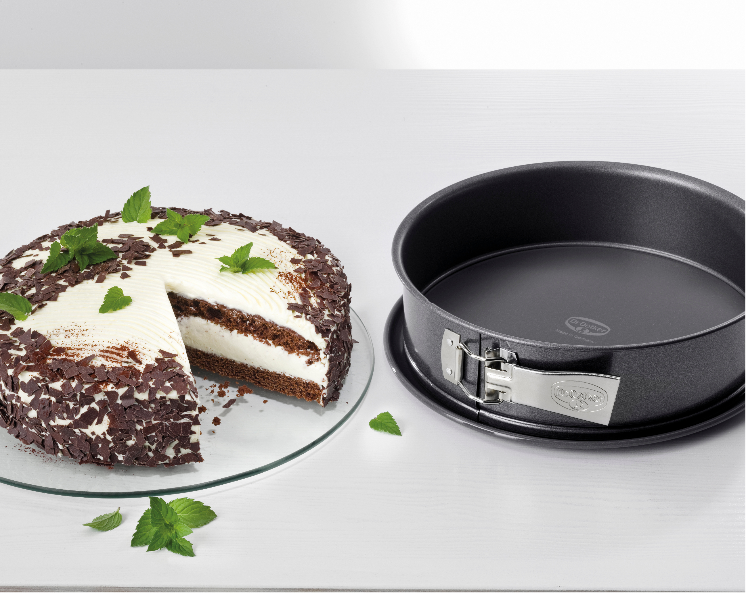 Ein Kuchen mit einem entfernten Stück, mit Schokolade und Minze verziert. Auf der rechten Seite ist eine Backform.