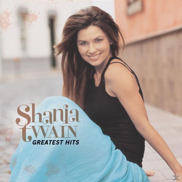 Shania Twain album borítója. Mosolyog, fekete felsőt és kék szoknyát visel. Cím: Greatest Hits.