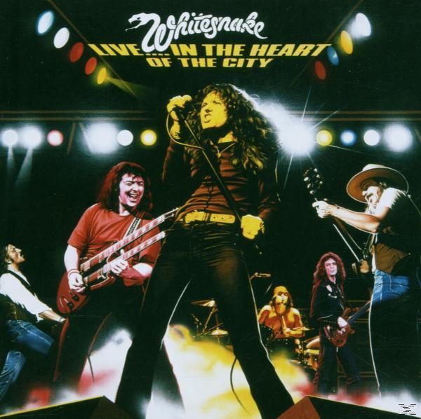 Whitesnake-Band live, Leadsänger am Mikrofon. Bühnenbeleuchtung und Bandmitglieder sichtbar.