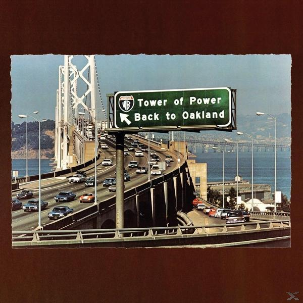 Híd autókkal, egy zöld tábla azt írja: „Tower of Power Back to Oakland”. Barna előtér, kék ég.
