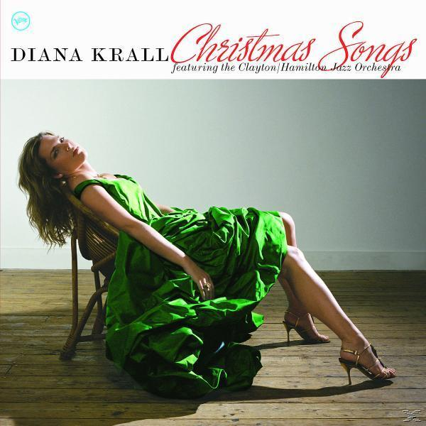 Nő zöld ruhában fotelben. Barna fa padló, világos háttér. Diana Krall 'Christmas Songs' album borítója.