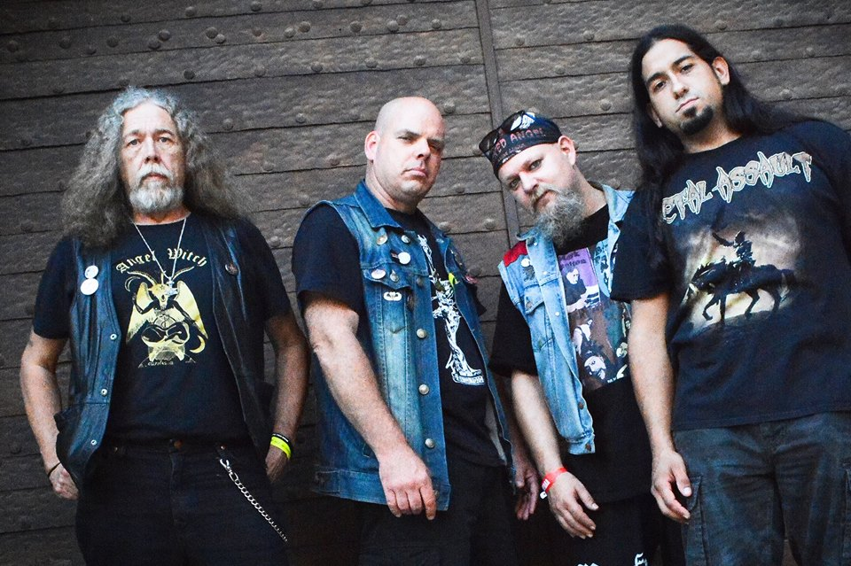 Metal-Band mit vier Mitgliedern in einem Gruppenfoto, das vor einer braunen Tür steht.