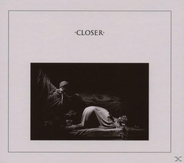 Monochromes Bild. Zwei Figuren in dunkler Umgebung, eine kniet, eine lehnt sich. Das Wort 'Closer'.