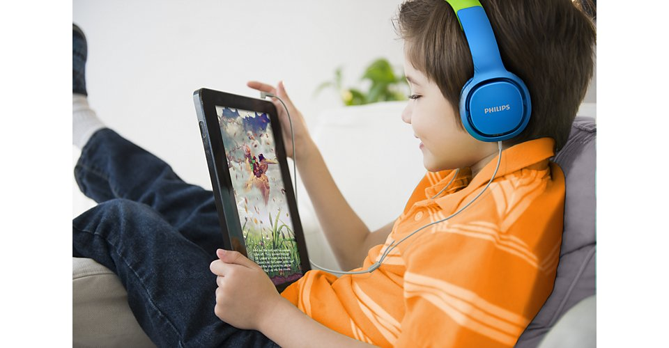 Een jongen met een blauwe koptelefoon kijkt naar een tablet. Hij draagt een oranje shirt en zit op een bank.