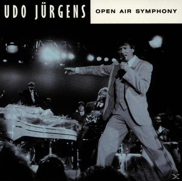 Udo Jürgens singt mit Mikrofon auf der Bühne. Bandmitglieder sind hinter ihm sichtbar.