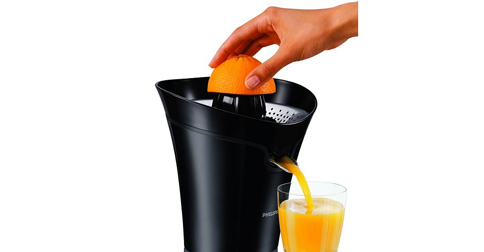 Une main presse une demi-orange dans un presse-agrumes noir, le jus coule dans un verre.