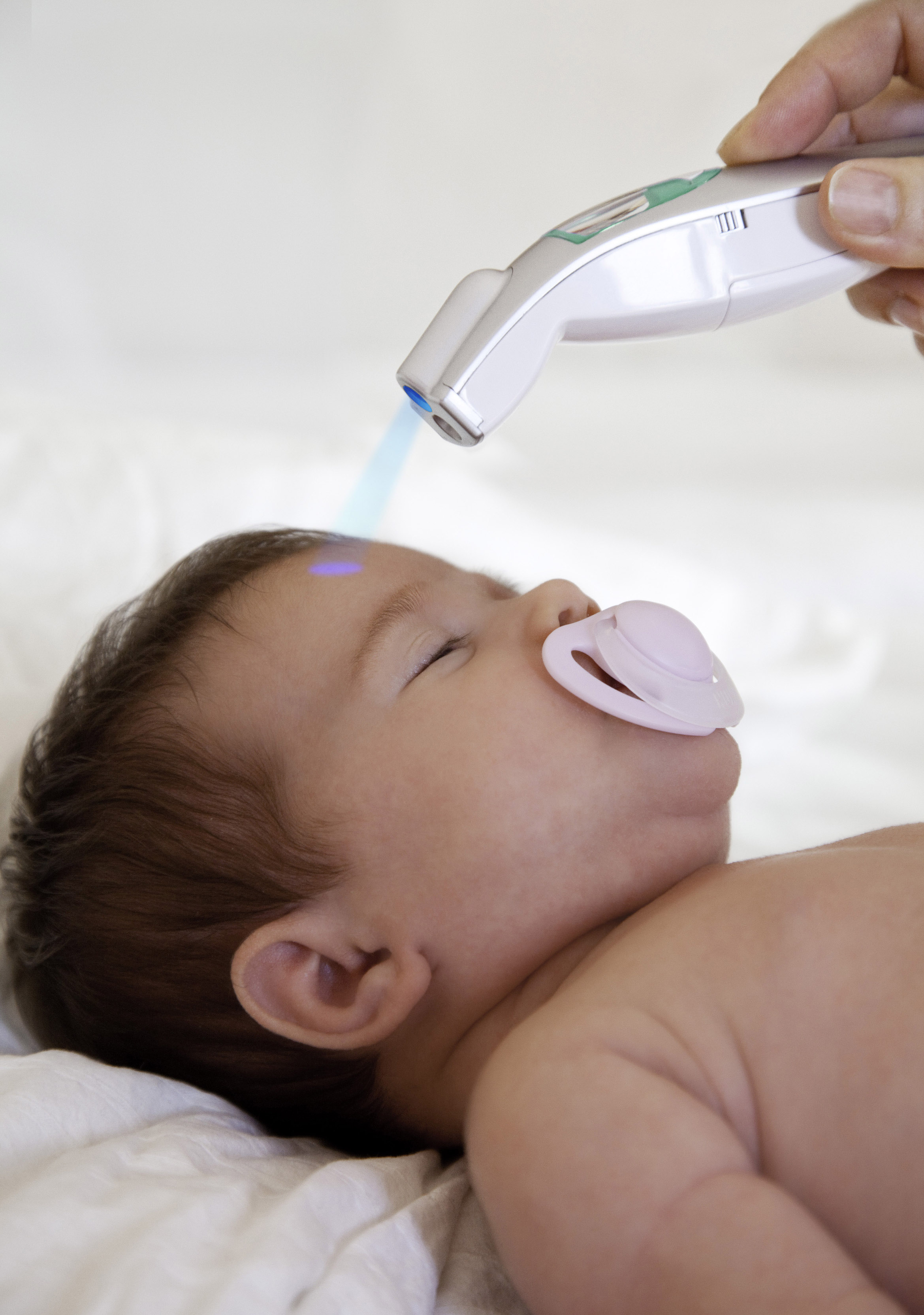 Ein Baby mit Schnuller hat blaues Licht auf der Stirn. Ein medizinisches Gerät wird über dem Kopf des Babys gehalten.