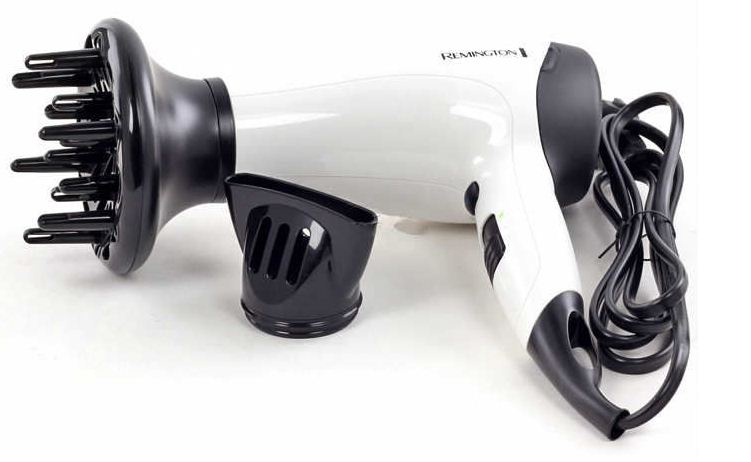 Un sèche-cheveux Remington blanc et noir avec un diffuseur et une buse est posé sur une surface blanche. Le cordon est enroulé.