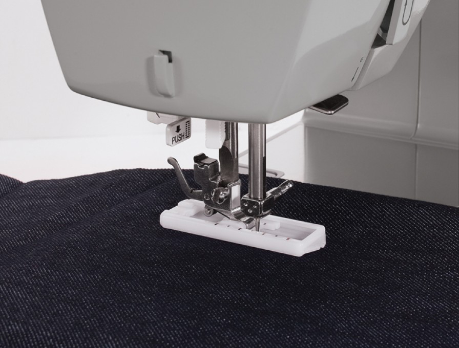 Sewing machine close-up. Needle and presser foot on dark blue fabric.