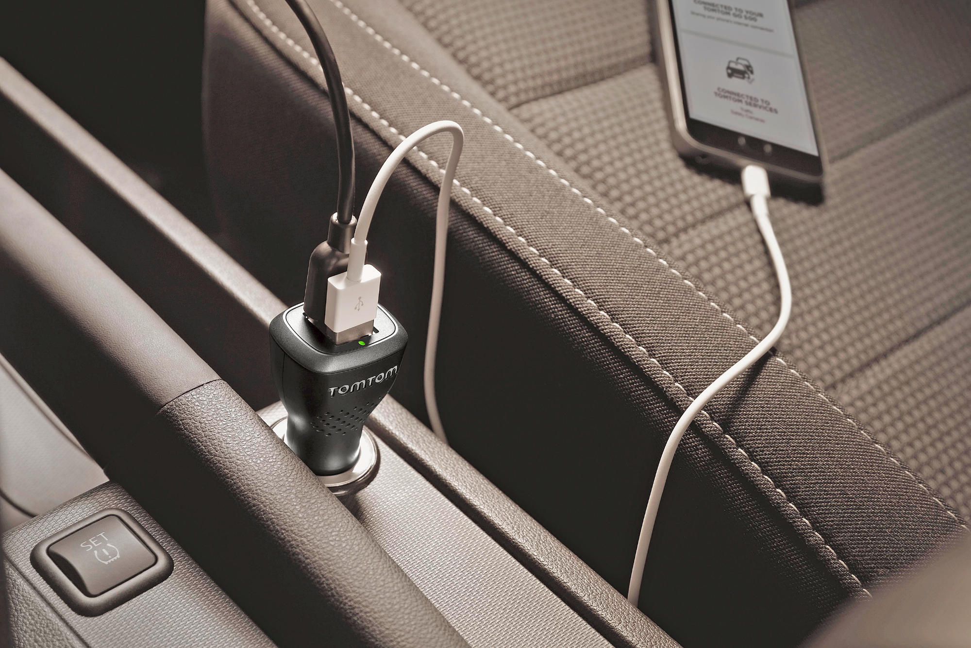 Ein Auto-Innenraum mit einem eingesteckten TomTom-Ladegerät. Ein Telefon ist mit dem Ladegerät verbunden.
