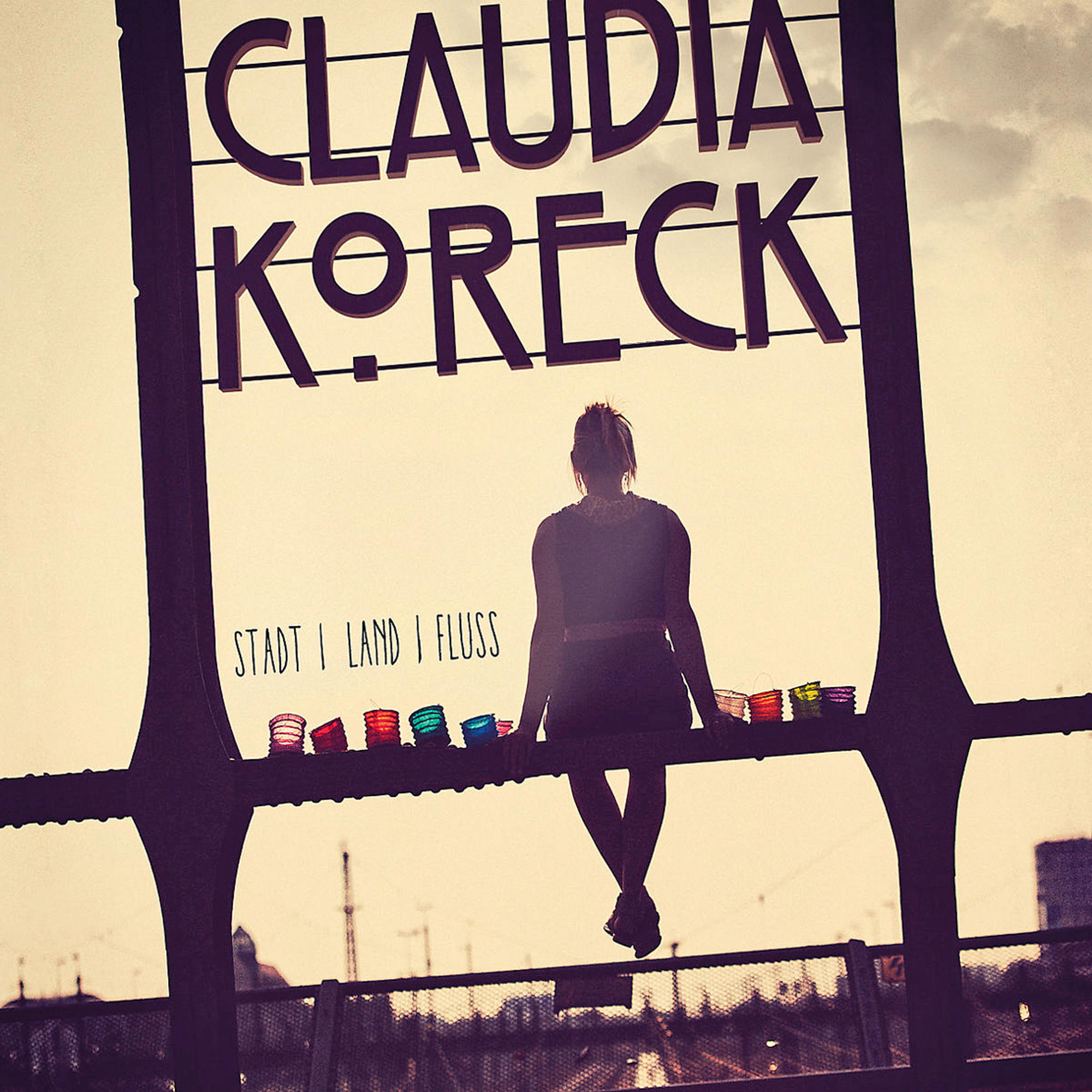Albumcover einer Frau, die auf einer Brücke sitzt, mit der Stadt im Hintergrund. Text: Claudia Koreck, Stadt, Land, Fluss.