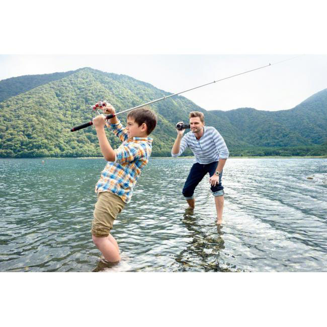Ein Junge fischt mit seinem Vater in einem See. Berge im Hintergrund.