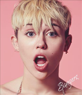 Miley Cyrus közeli képe rövid szőke hajjal, tátott szájjal és meglepett arcifejezéssel rózsaszín háttér előtt.