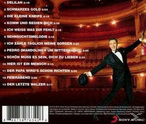 Ein Mann im Smoking posiert auf einer Bühne. Im Hintergrund ein Theater mit roten Vorhängen. Titelliste links.