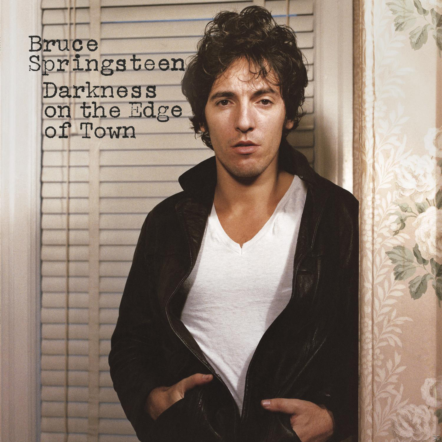 Bruce Springsteen Albumcover. Er steht, trägt eine Jacke und ein weißes V-Ausschnitt-Shirt, schaut in die Kamera.