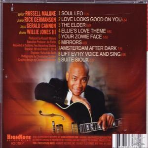 CD-Cover mit einem Mann, der Gitarre spielt, Text und Titelliste an der Seite. Dunkler Hintergrund.