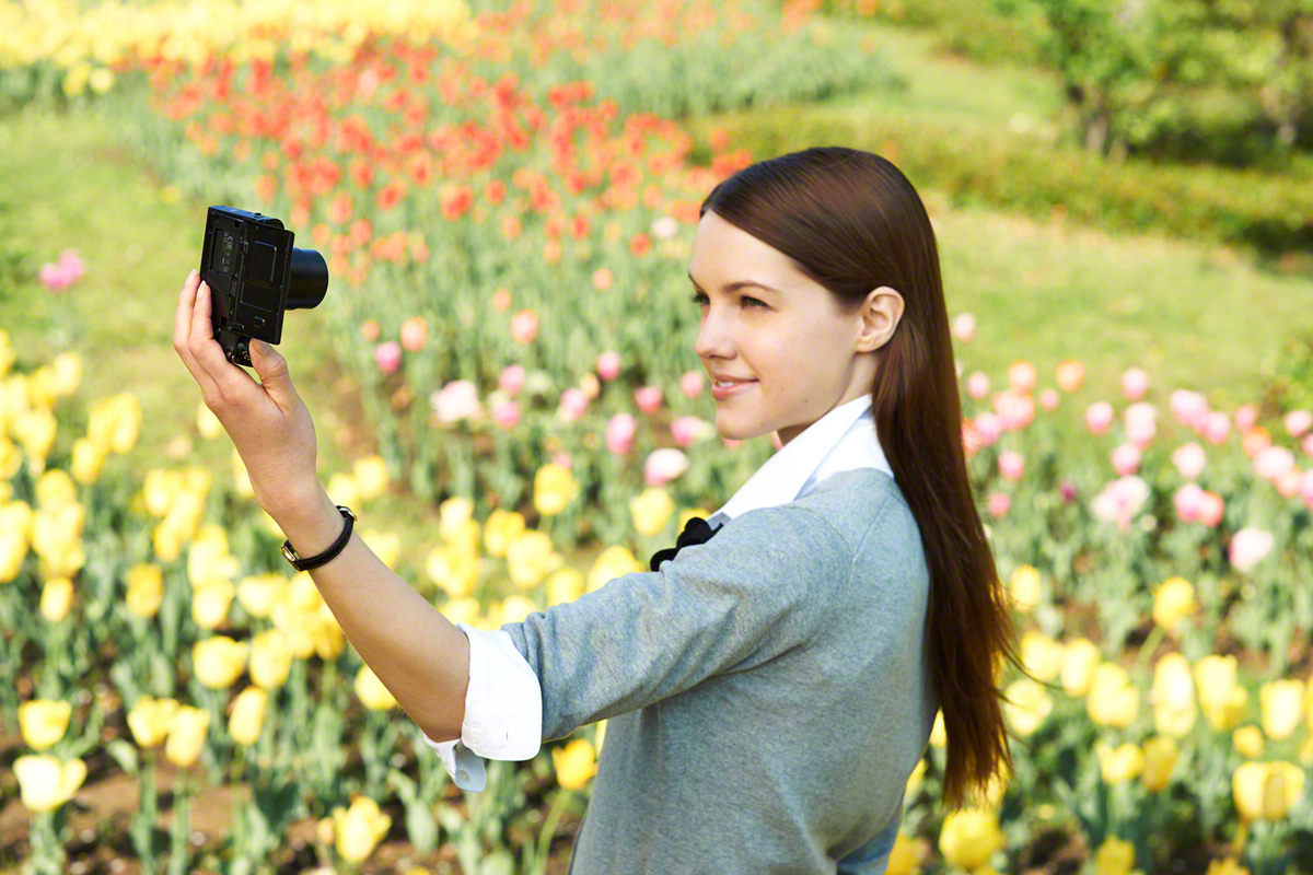 Femme prenant un selfie avec un appareil photo dans un champ de fleurs jaunes et rouges.