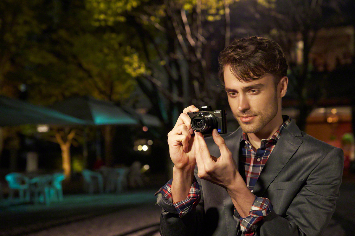 Un homme prend une photo avec un appareil photo Sony la nuit. L'arrière-plan comporte des arbres et un patio ouvert.