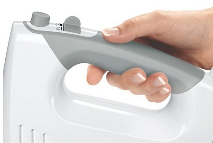 Een hand die een witte en grijze handgreep van een witte mixer vasthoudt. De mixer heeft een snelheidsregeling.