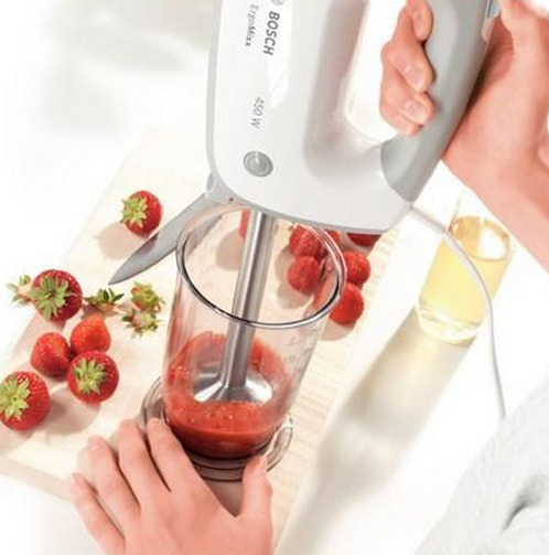 Une personne utilise un mixeur plongeant Bosch pour mélanger des fraises dans un verre.