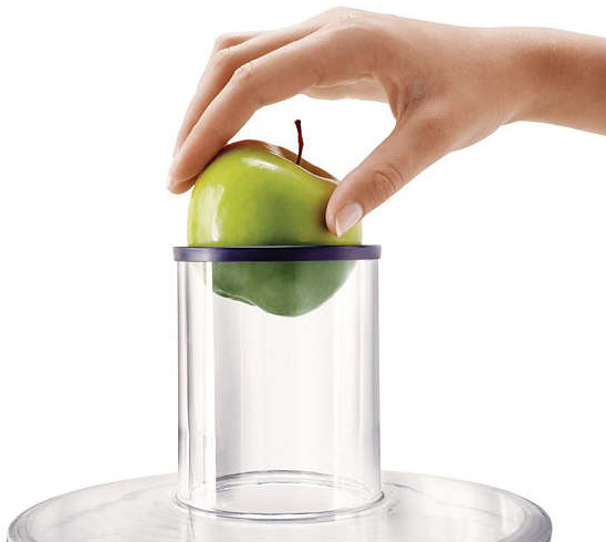 Hand die een groene appel in een transparante plastic appelboor plaatst, op een witte achtergrond.