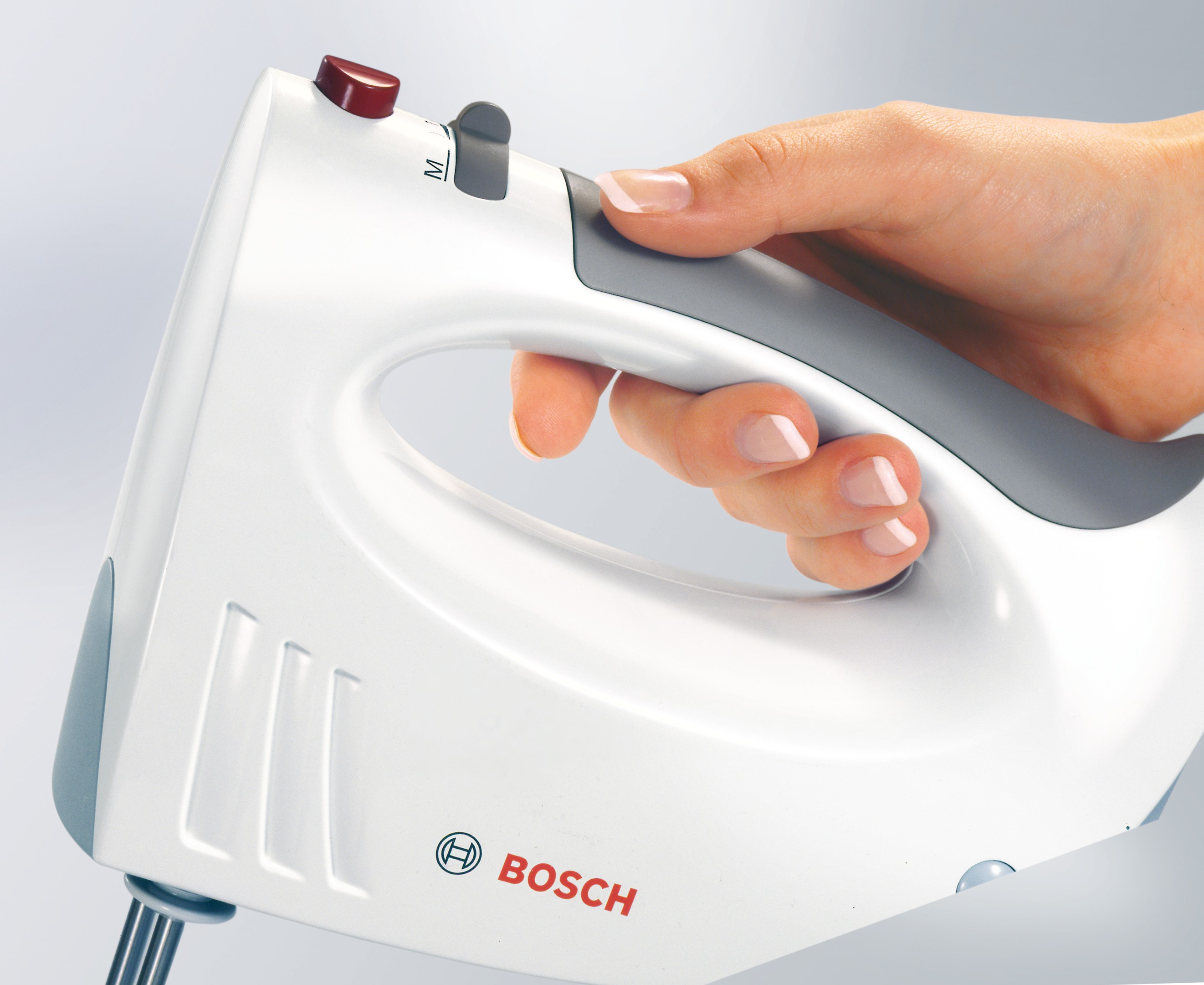 Main tenant un batteur à main blanc avec une poignée grise. Le logo Bosch est visible.