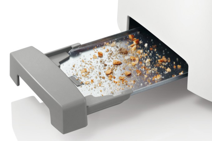 Nahaufnahme einer Toaster-Krümelschublade. Die Schublade ist voller Brotkrumen. Der Toaster selbst ist weiß und grau.