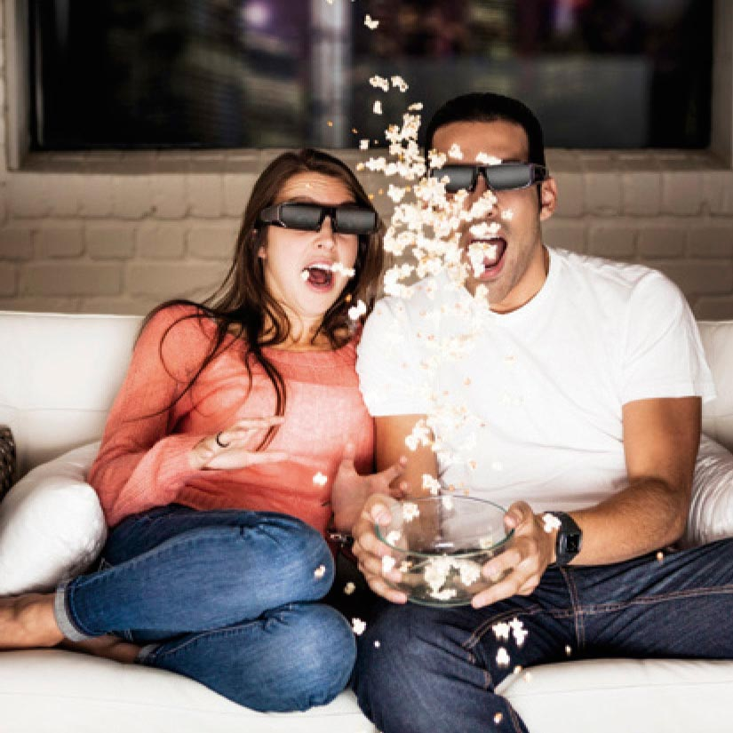 Een stel met een 3D-bril, geschrokken van popcorn die uit een kom komt.