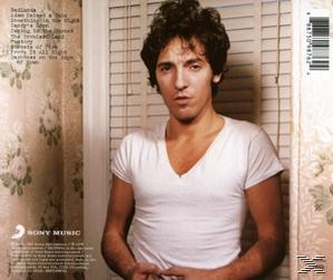 Albumcover mit Bruce Springsteen im weißen T-Shirt, stehend vor einer gemusterten Wand.