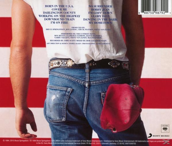Rug van een man in jeans en een wit shirt met albumcovertekst, rode pet in de zak.