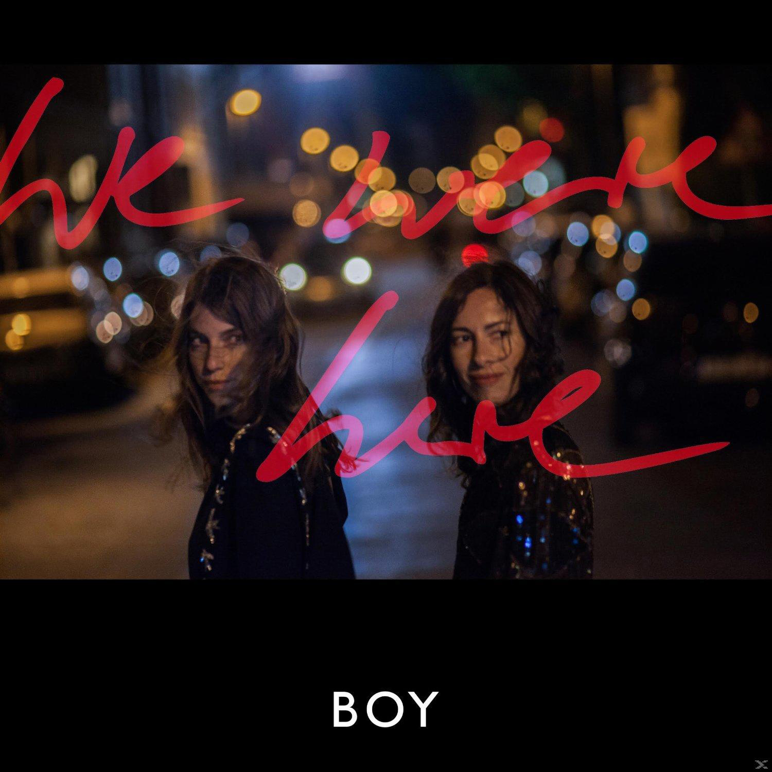 Zwei Frauen auf der Straße mit Bokeh-Lichtern, das Wort 'we are here' in Rot.