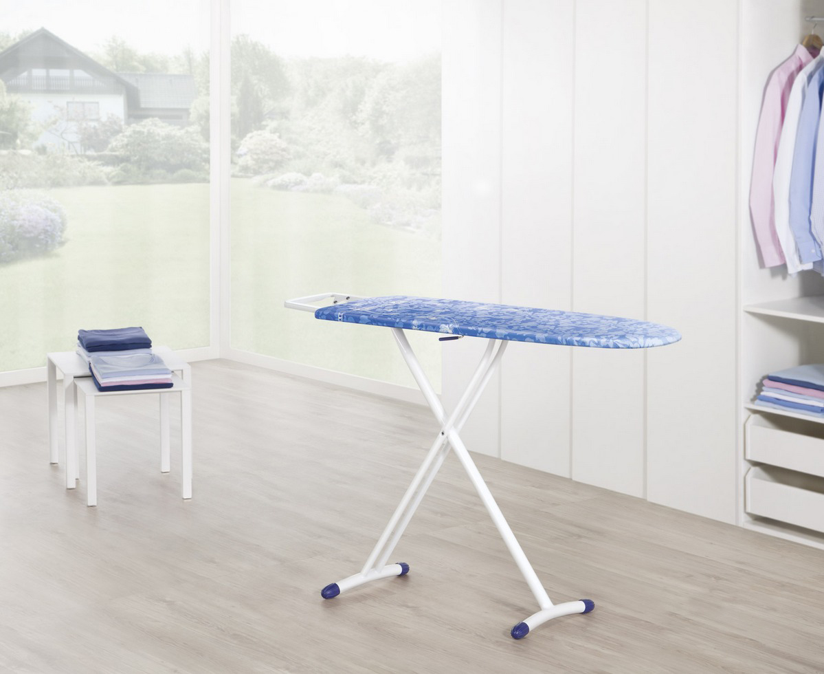 Une table à repasser, des vêtements et un placard dans une pièce lumineuse.